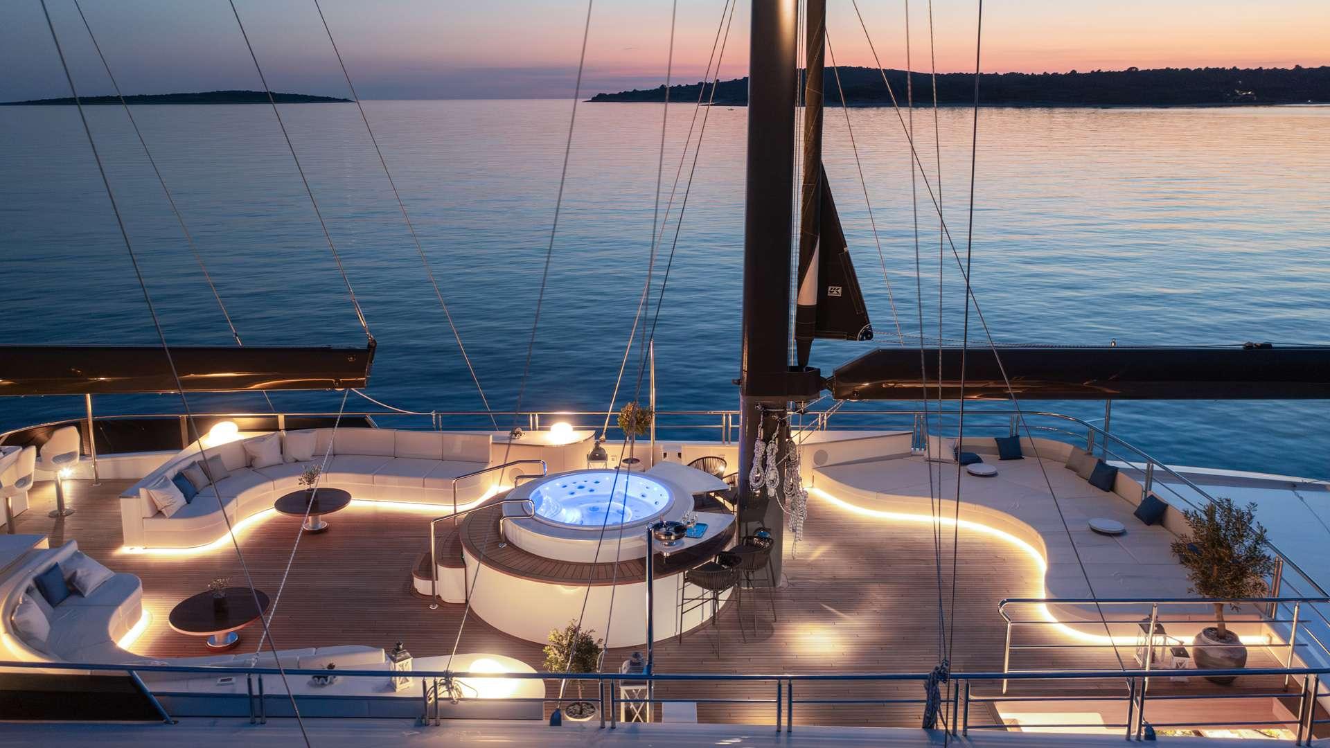 circular jacuzzi with blue lighting on yacht deck surrounded by seating areas at sunset
