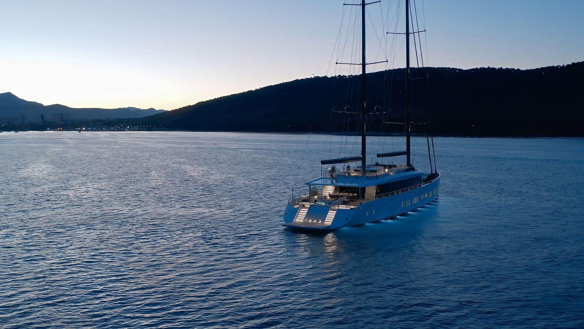 Blue hull luxury gulet with two masts anchored in peaceful bay surrounded by hills
