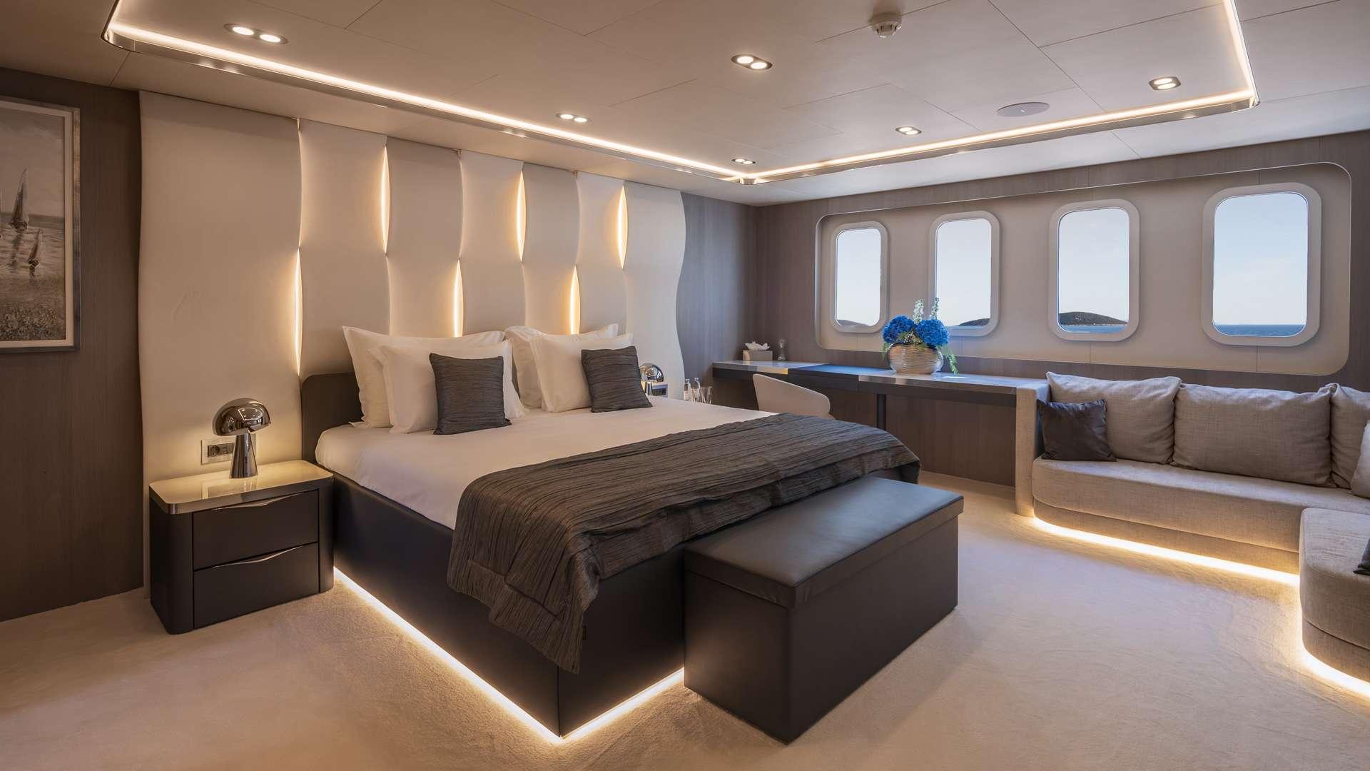 Master cabin featuring king bed with built-in nightstands, seating area and four hull windows