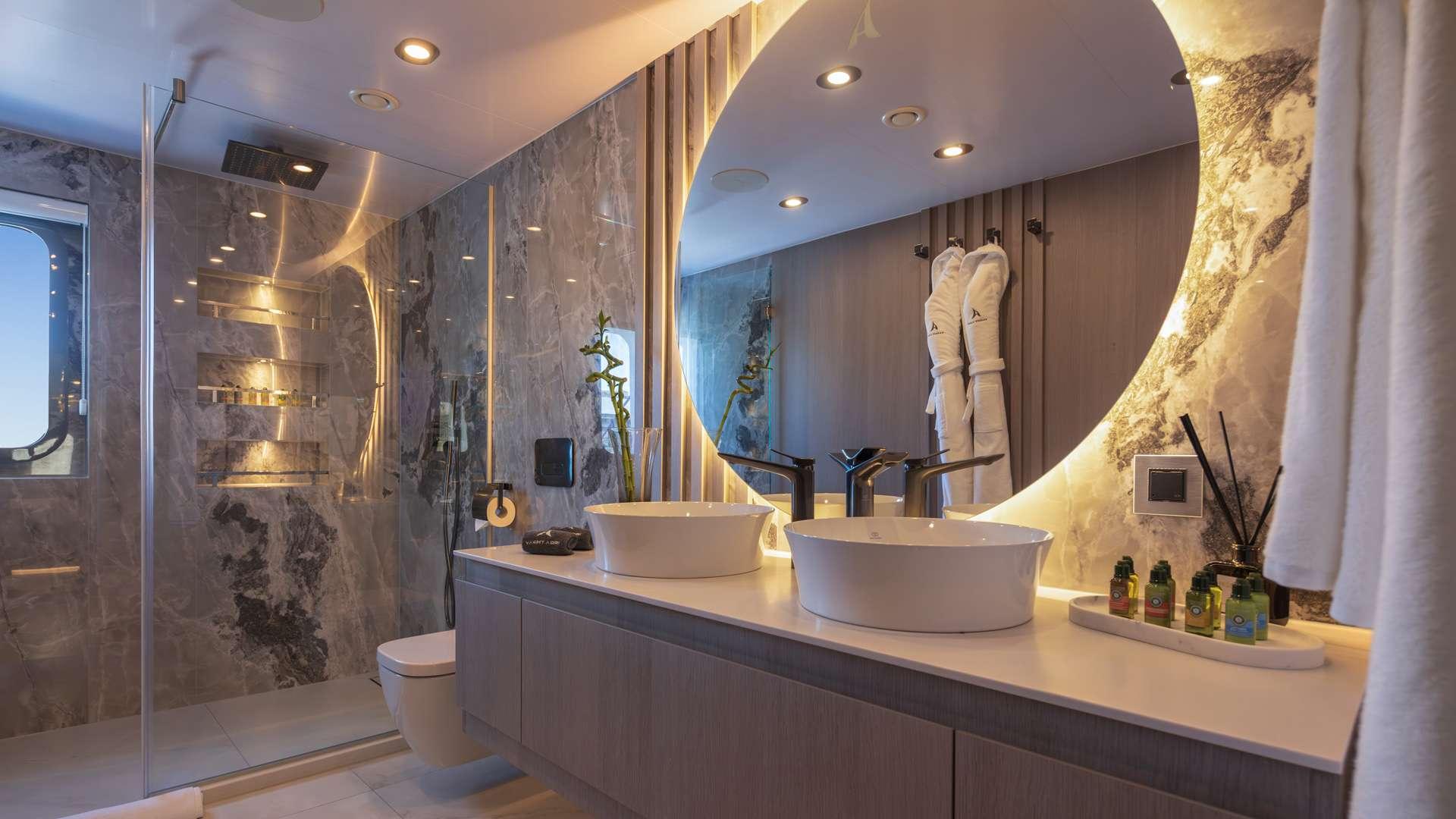 modern yacht bathroom featuring marble-clad walk-in shower, double vessel sinks, and ambient lighting
