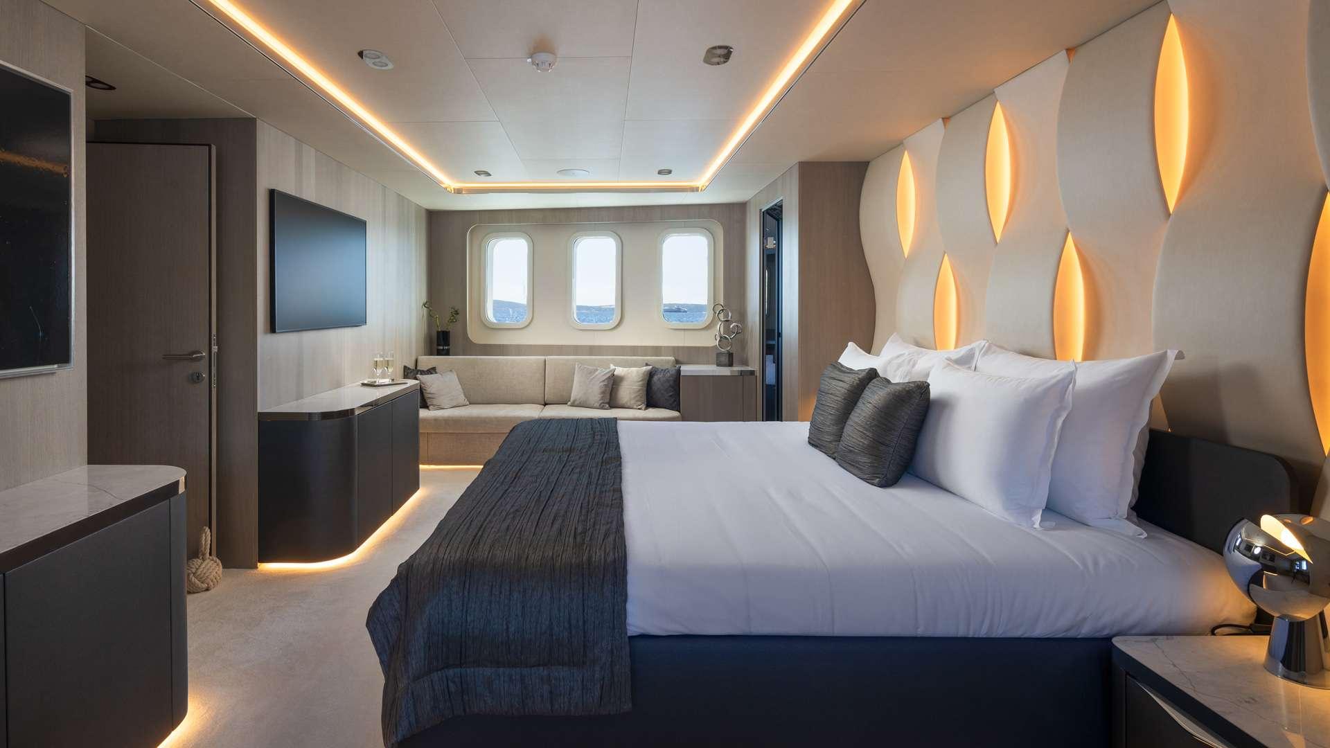 spacious yacht cabin featuring double bed, built-in seating area with portholes and decorative wall lighting