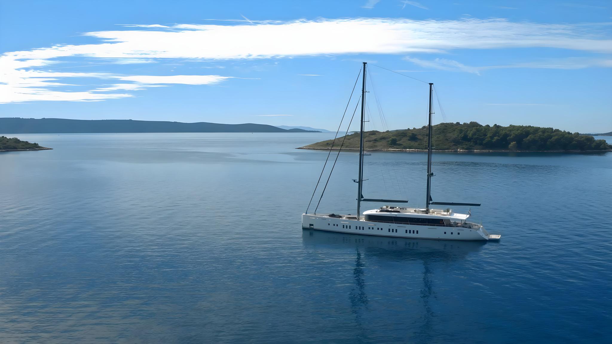 white luxury sailing yacht with two masts anchored in crystal blue Mediterranean waters near forested coastline