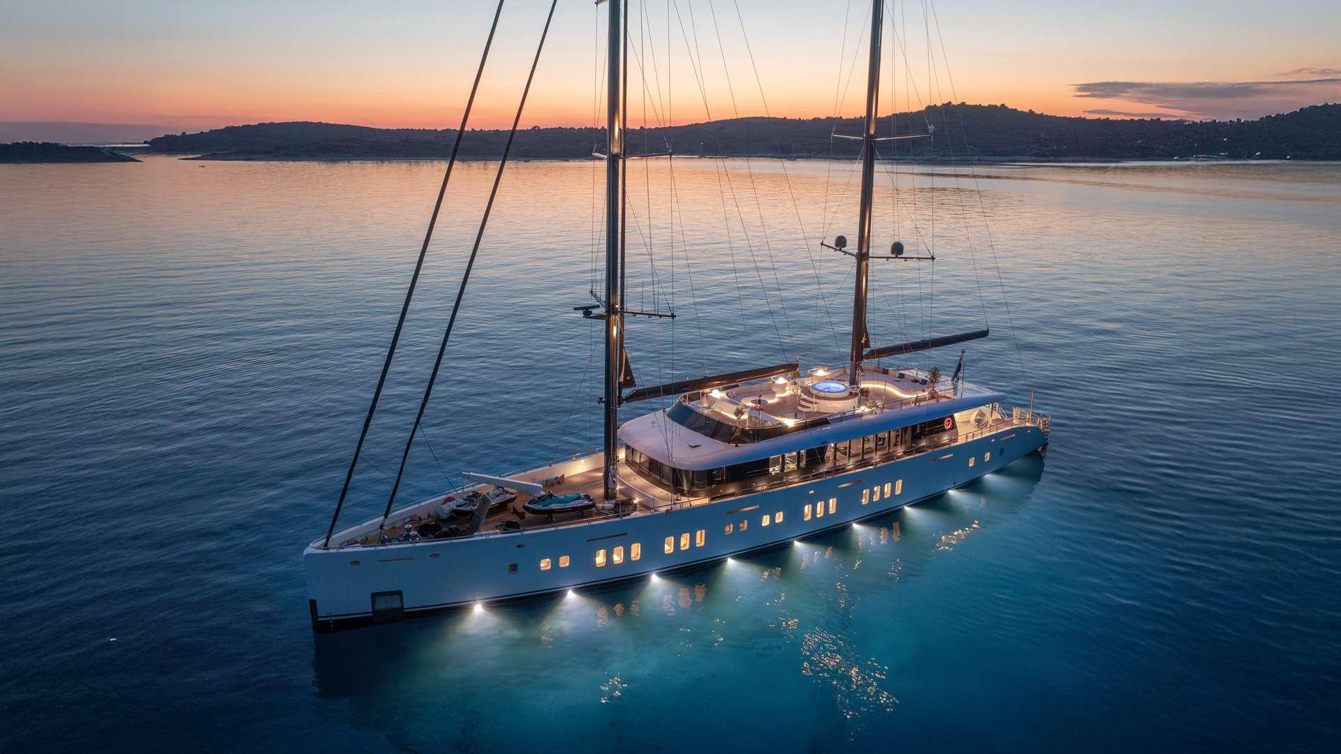 white sailing yacht with illuminated windows anchored in calm bay at sunset