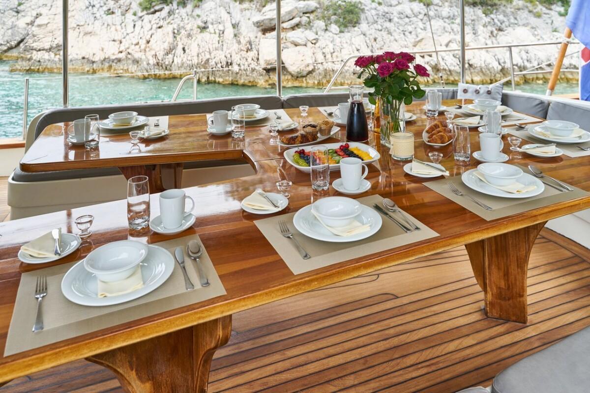 yacht outdoor dining table set with food, roses, and Mediterranean coastline view