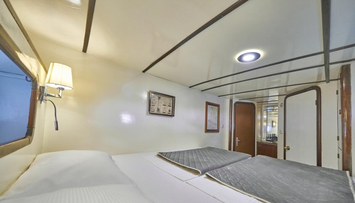 Twin bed yacht cabin with white linens, porthole window, reading lamp