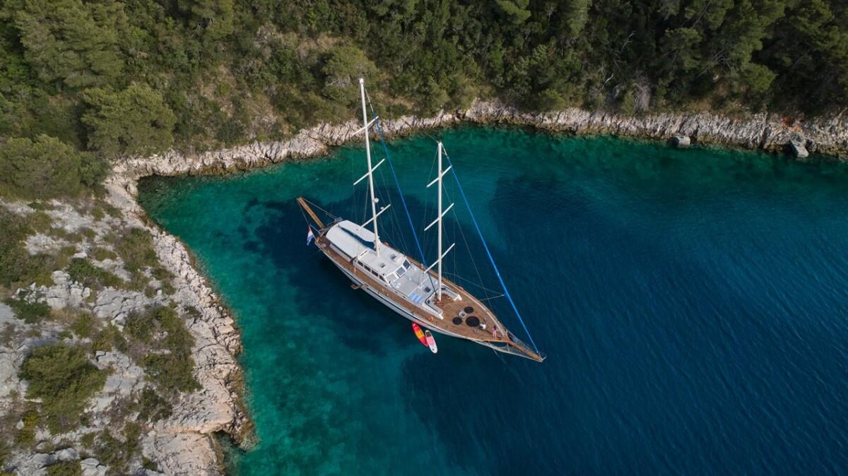 Traditional wooden gulet yacht anchored in pristine turquoise Mediterranean bay aerial view