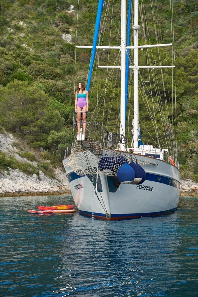 White sailing yacht Fortuna anchored in blue water with woman on bow