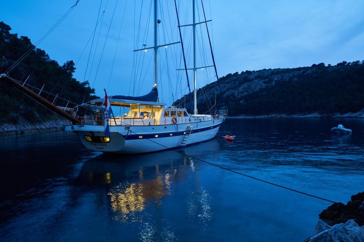 White gulet with two masts anchored in peaceful cove during blue hour