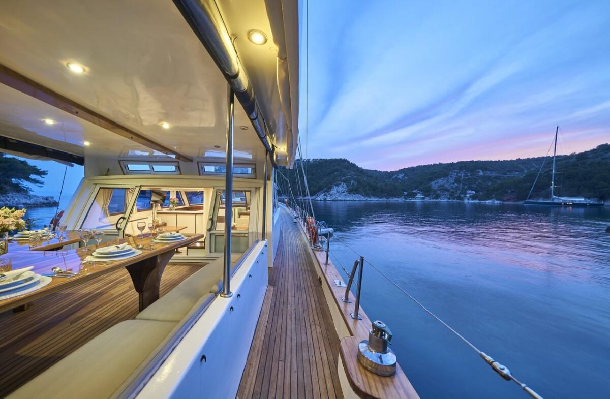 Luxury yacht side deck with teak flooring and illuminated dining salon at twilight