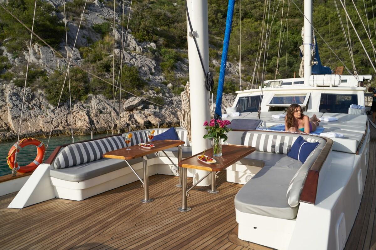 luxury yacht aft deck with white seating, wooden table and coastal backdrop