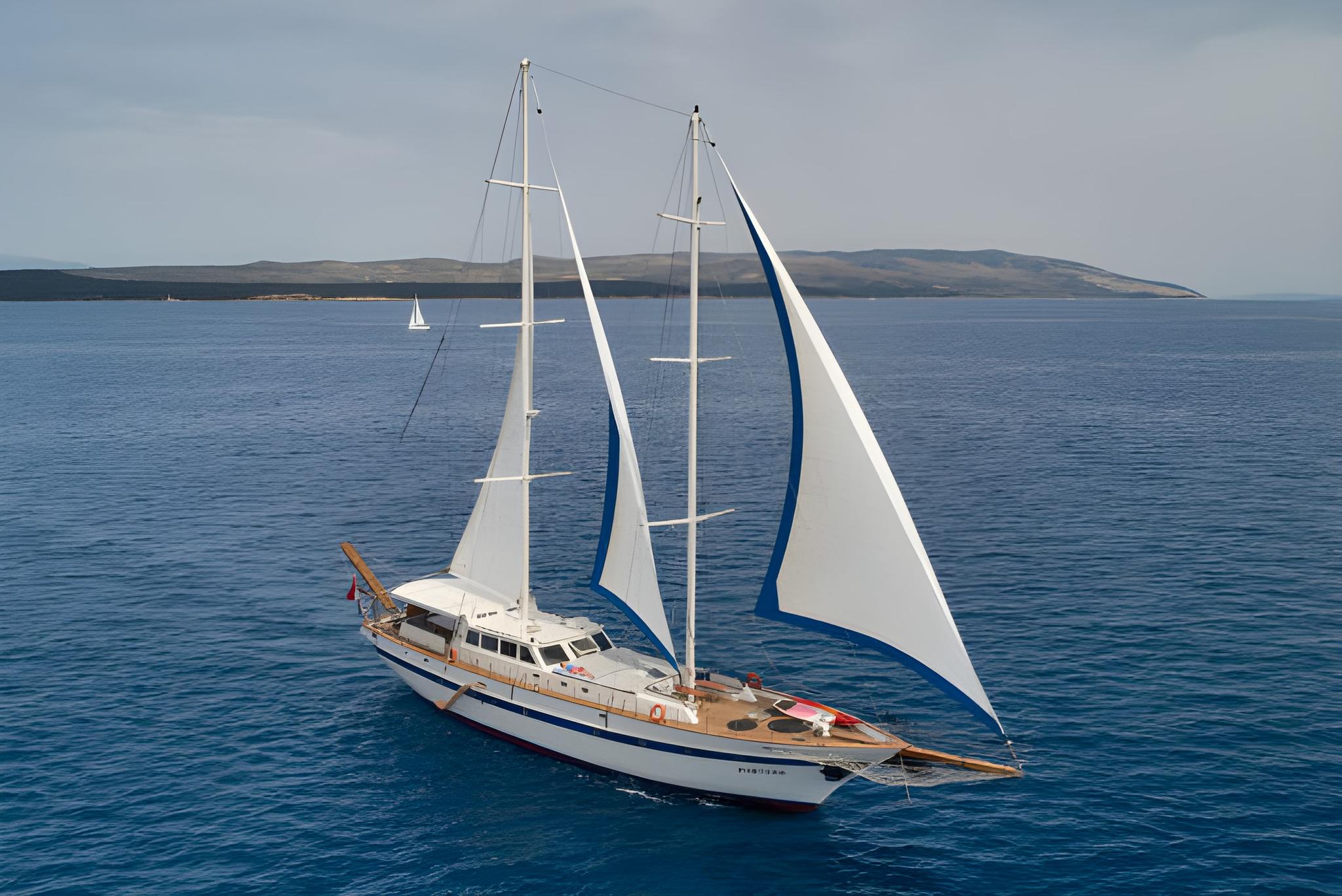 Aerial view of white-hulled sailing yacht with deployed sails on blue water