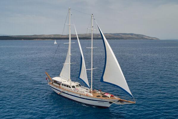 Aerial view of white-hulled sailing yacht with deployed sails on blue water