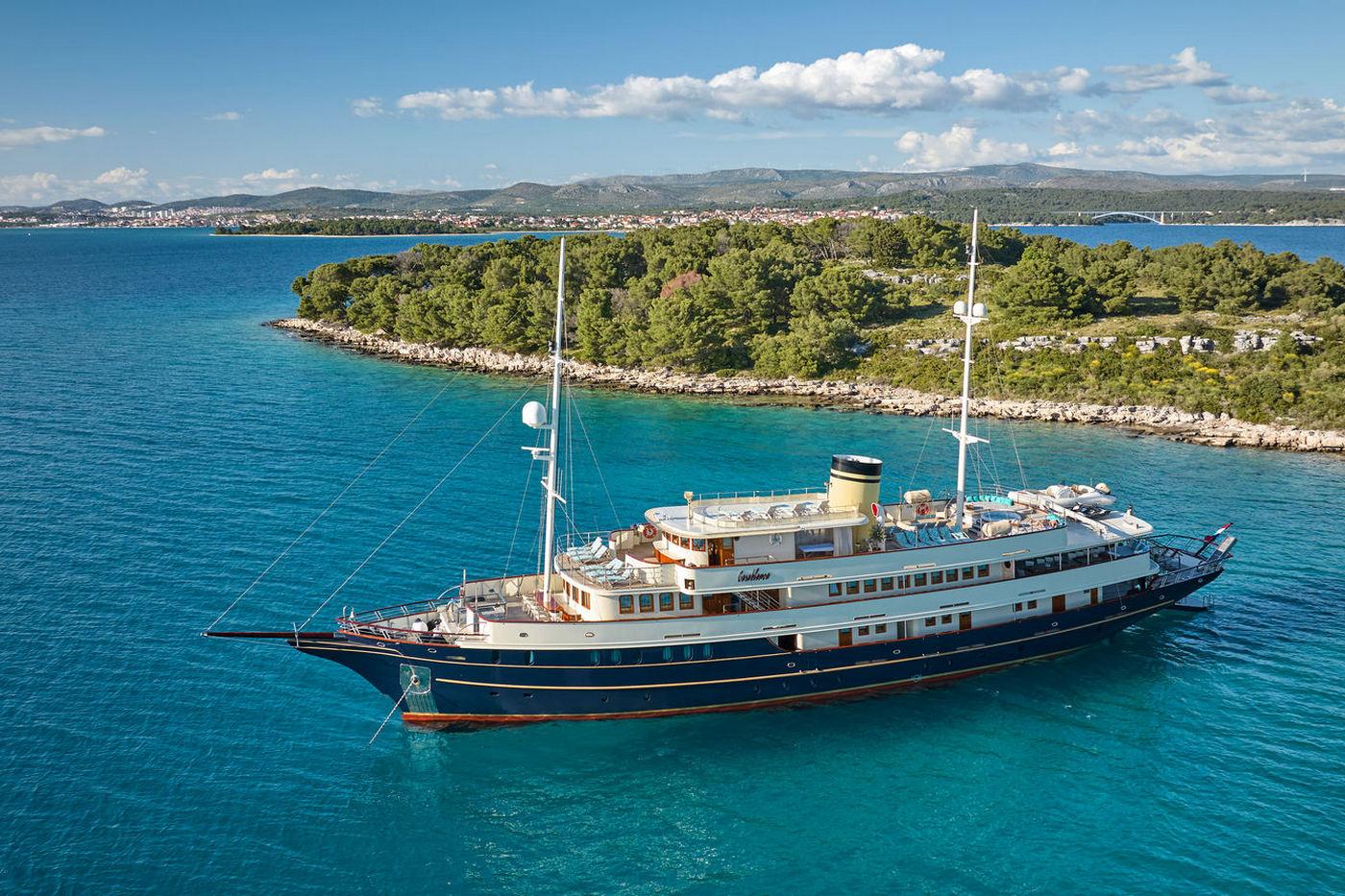 Large white motor yacht with yellow funnel anchored in crystal clear turquoise waters