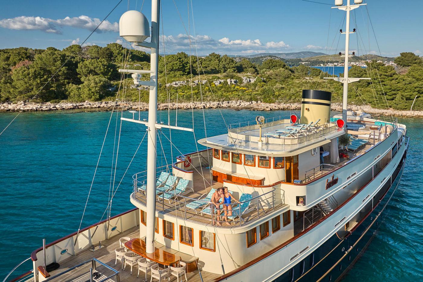 Traditional motor yacht with white hull and red trim anchored in crystal clear turquoise waters