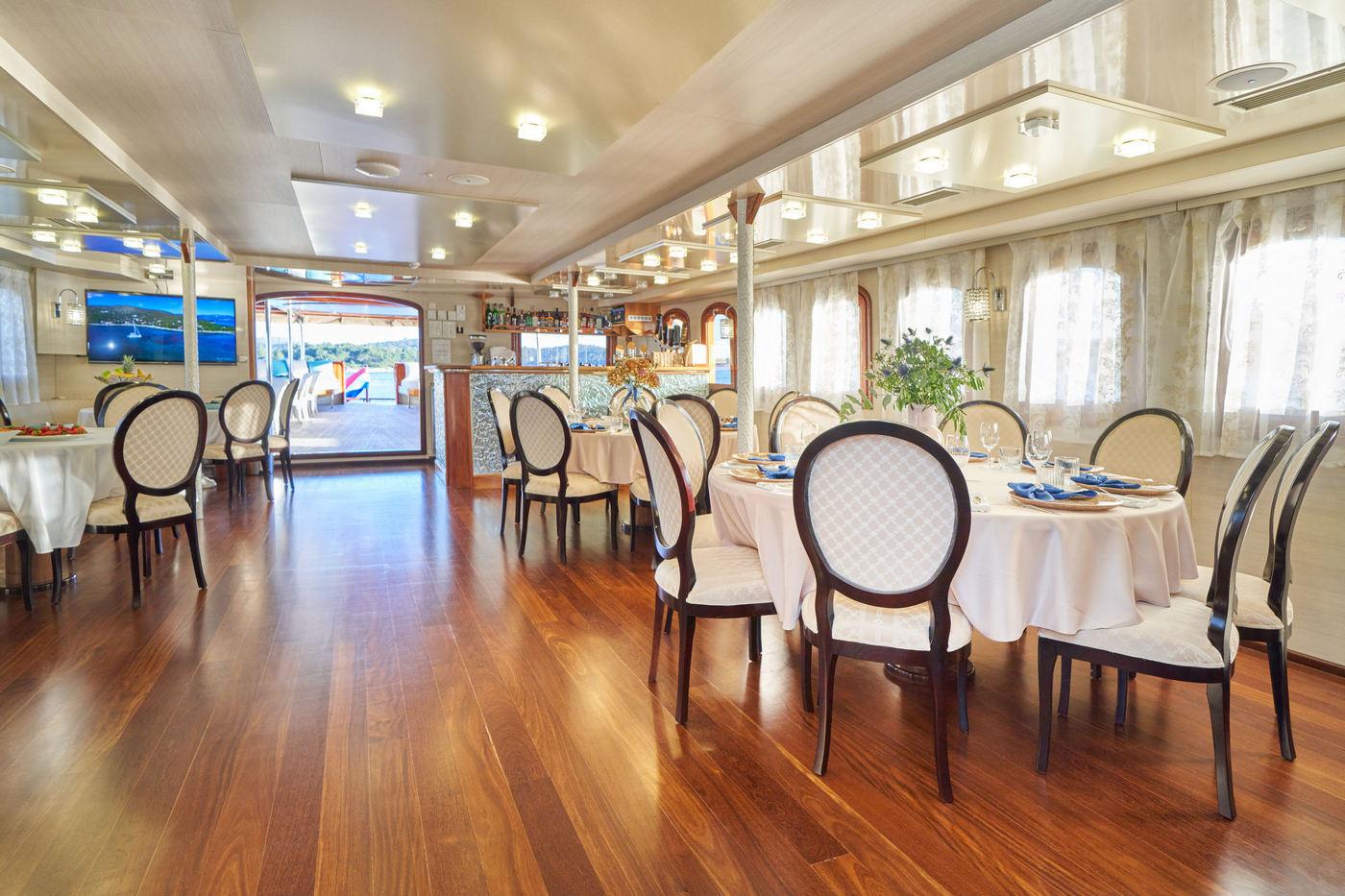 Luxury yacht dining salon with white tablecloths and quilted chairs