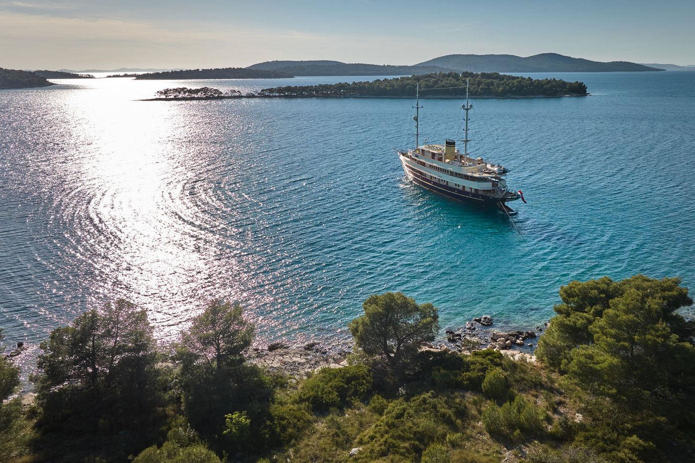Large white luxury yacht anchored in crystal clear turquoise Mediterranean bay