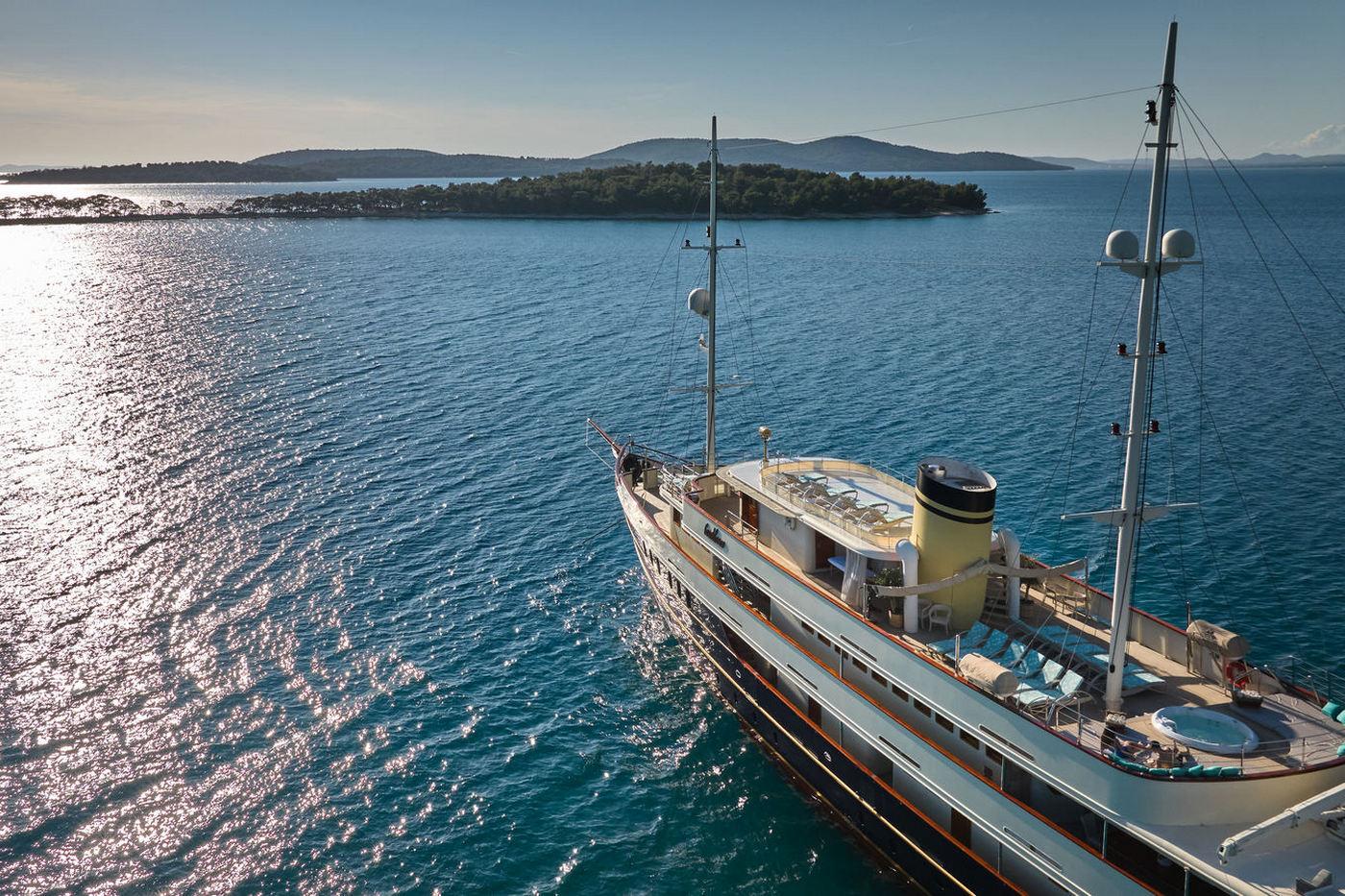 Aerial view of traditional motor yacht with cream hull anchored near forested islands