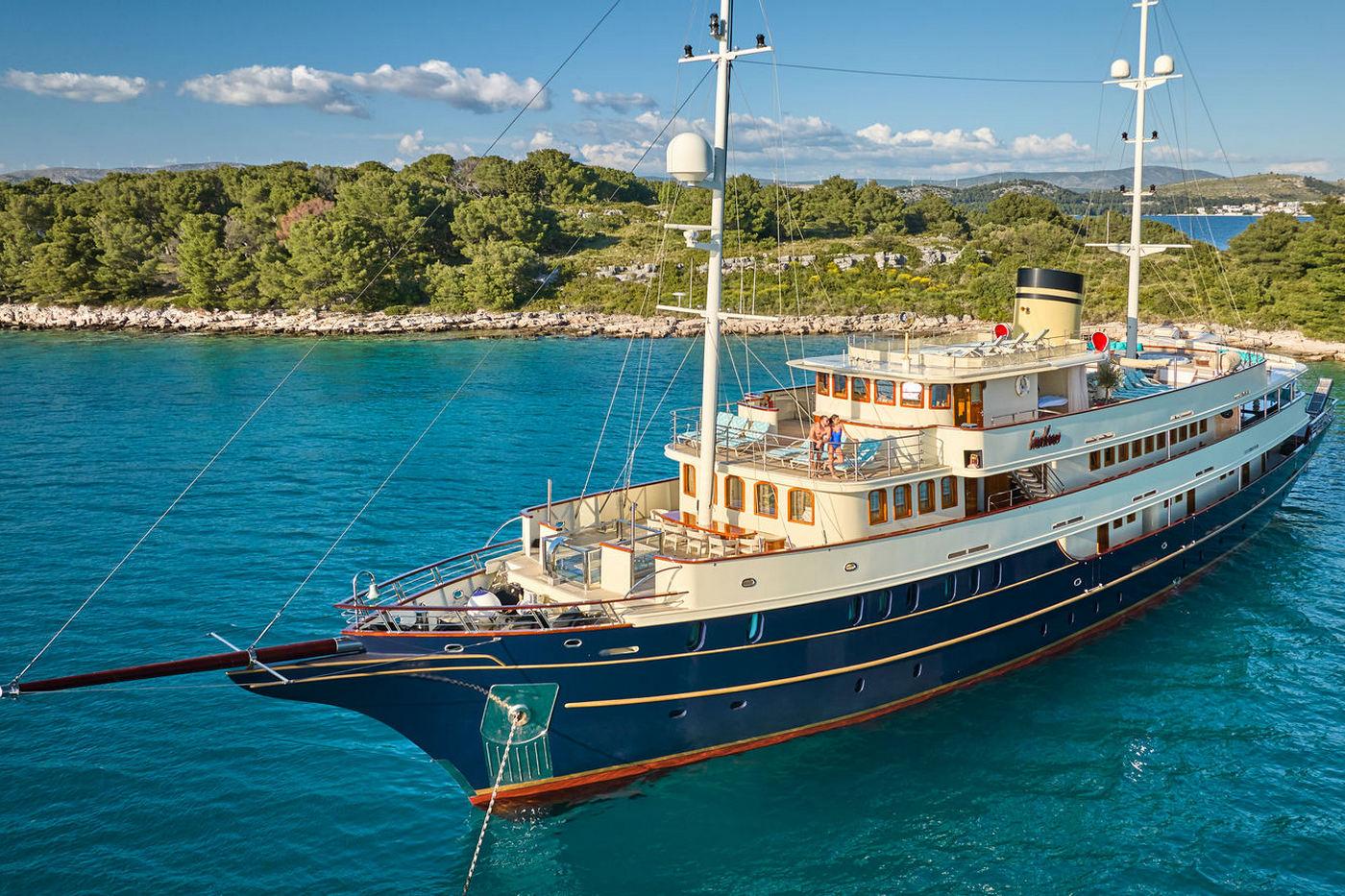 White classic motor yacht with dark blue hull anchored in crystal clear turquoise bay