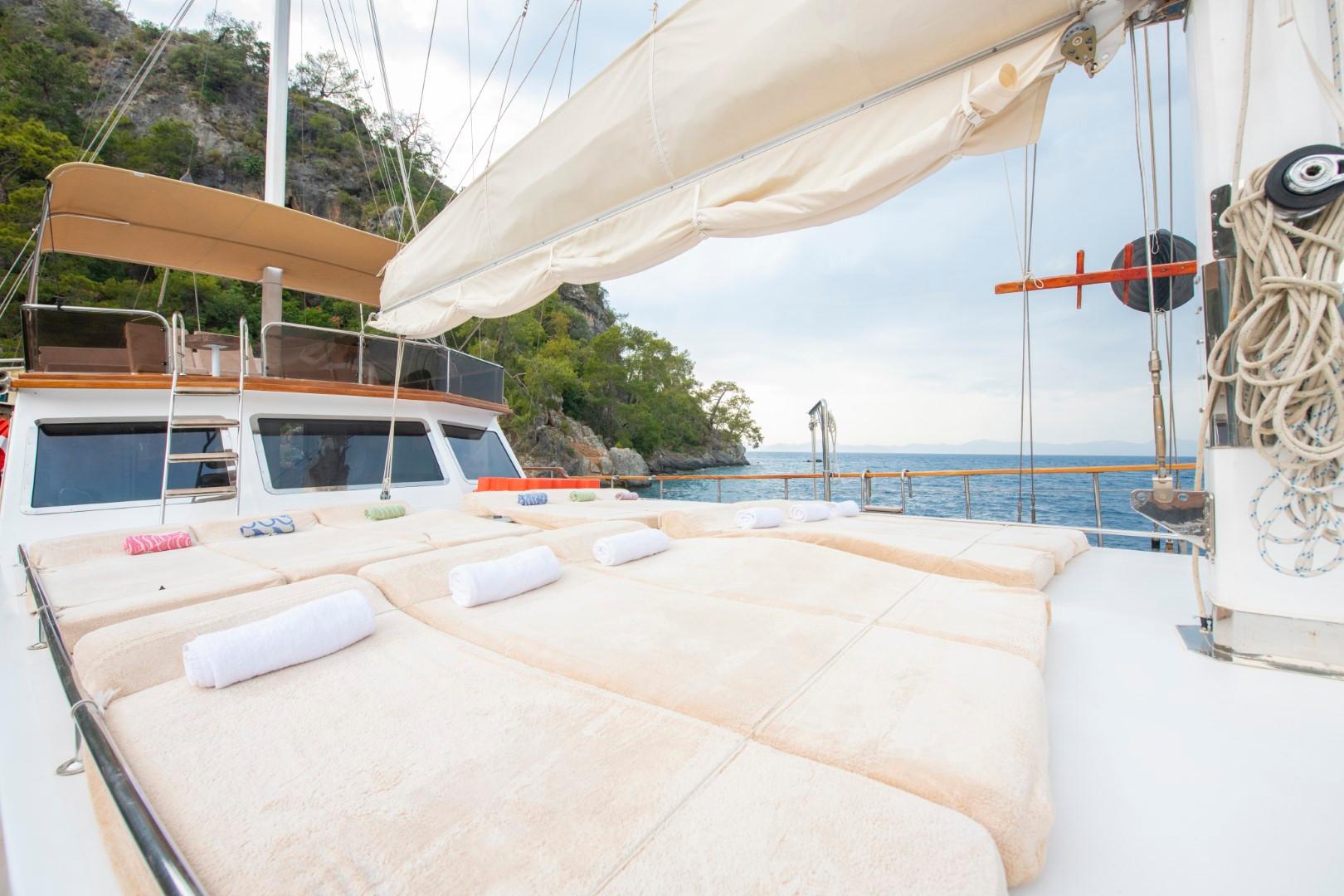 Gulet bow sun deck with cream cushioned loungers under beige sail awning in Mediterranean bay