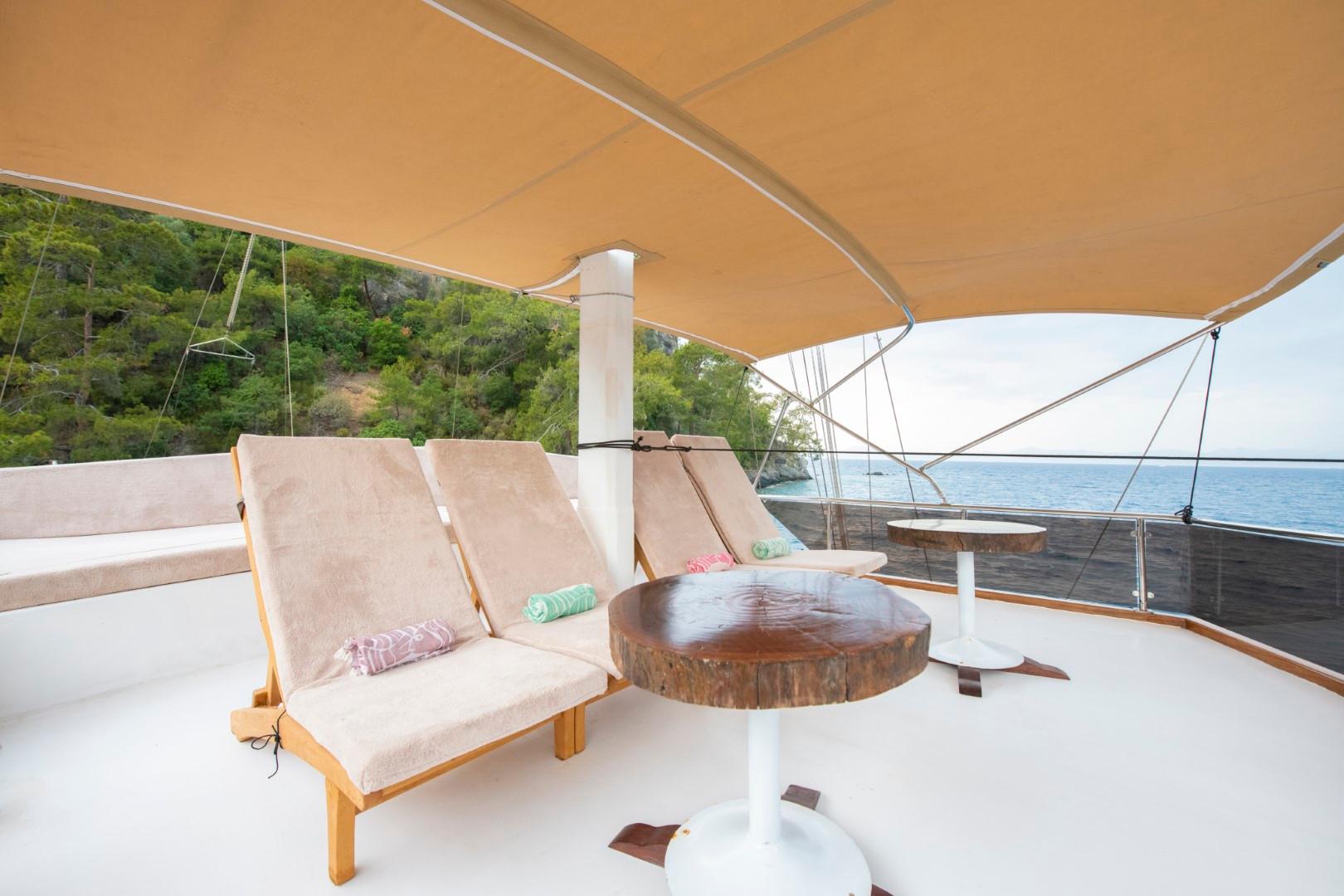 upper deck seating area with beige sun loungers, round wooden table and white umbrella