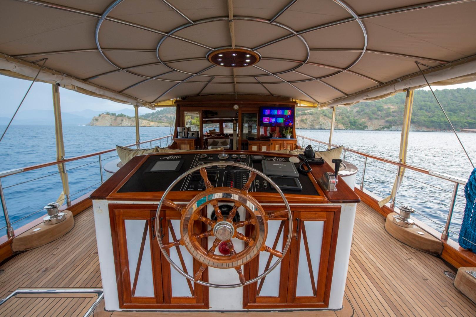 yacht wheelhouse with wooden steering wheel, navigation instruments, and coastal scenery