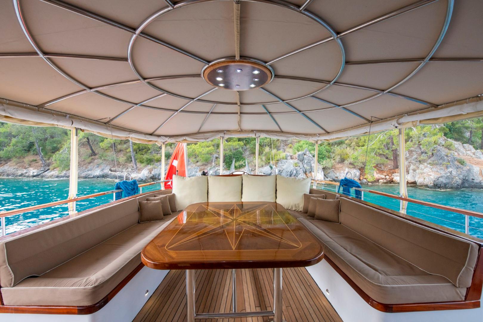 covered aft deck with U-shaped seating, wooden table, and coastal views