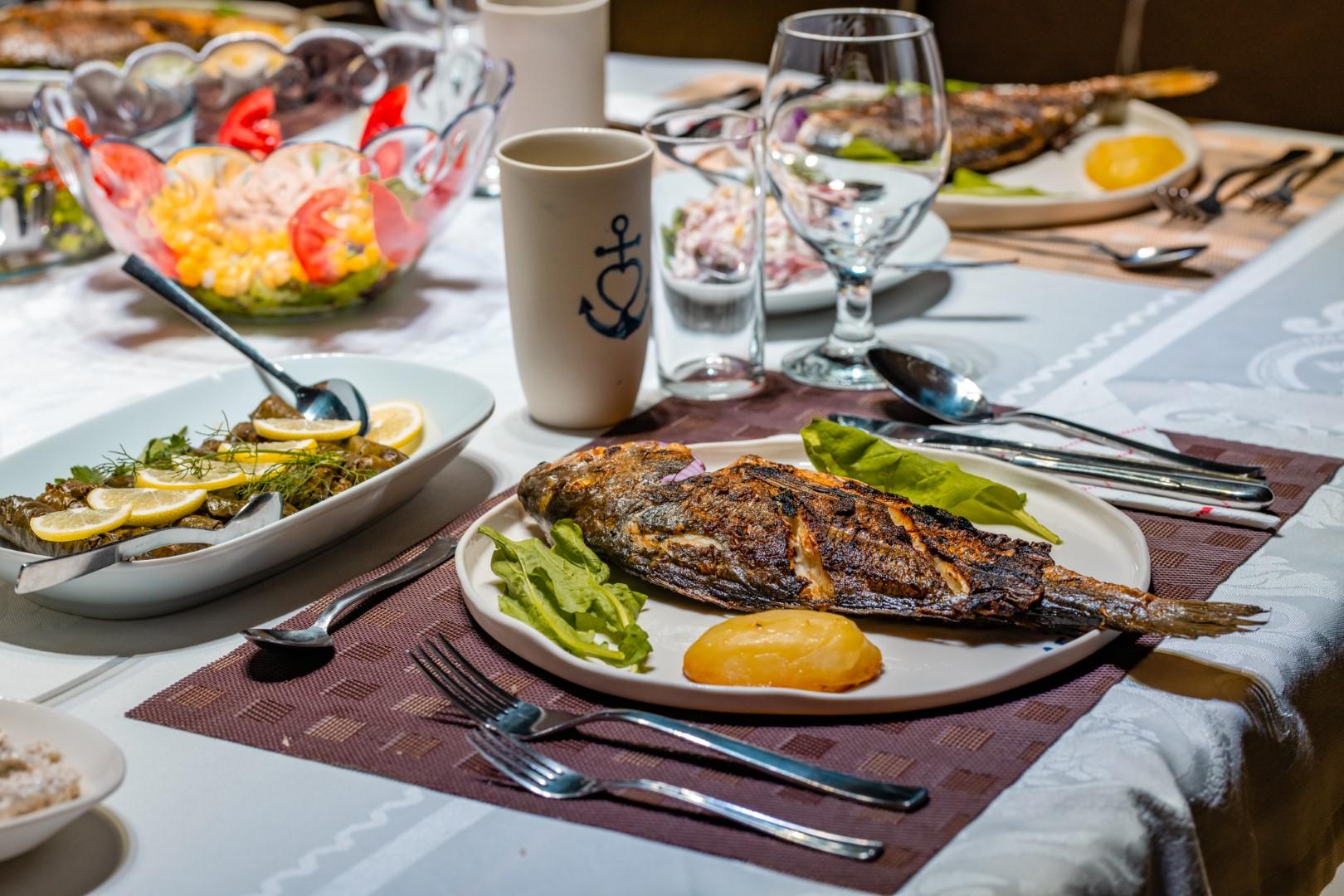 grilled whole fish with lemon and salad served on yacht dining table with wine glasses