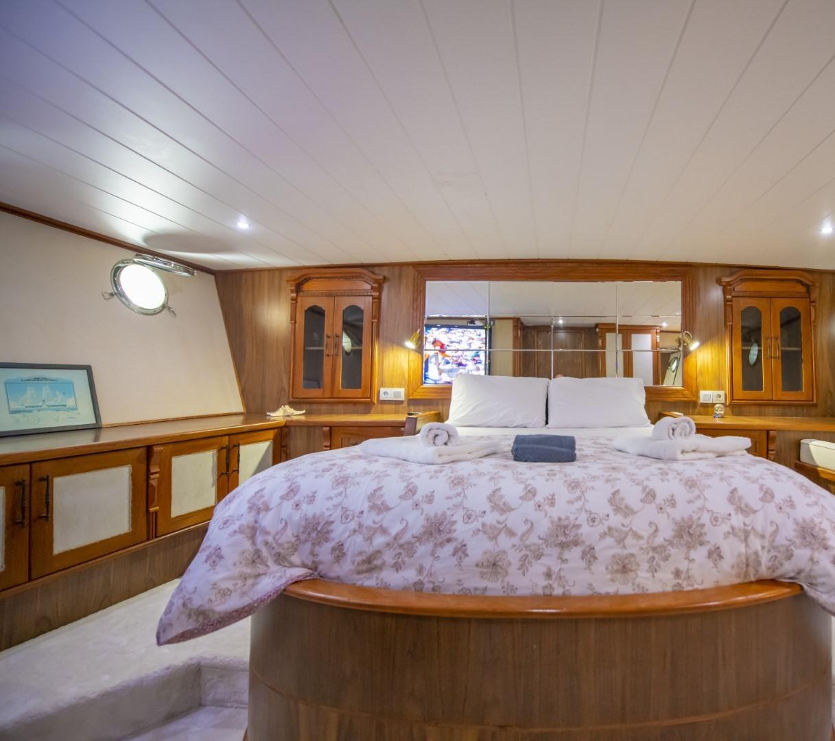 yacht cabin interior with double bed, wooden cabinetry, porthole window and white paneled ceiling
