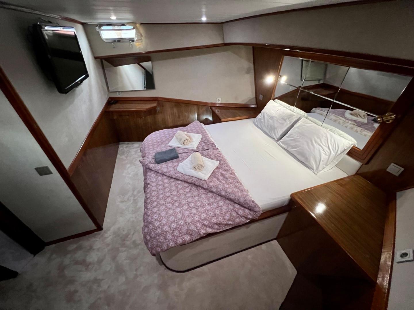yacht guest cabin with double bed, purple bedding, wall-mounted TV and mirrored headboard