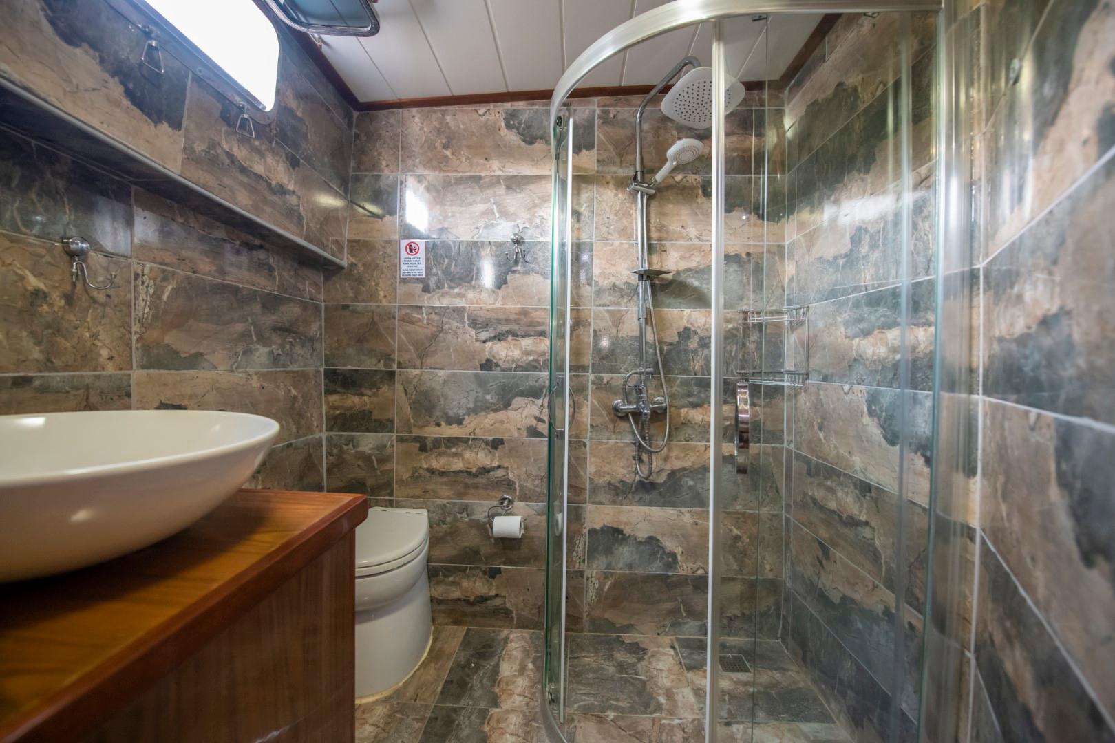 yacht bathroom featuring marble-effect tiled walls, glass shower enclosure, white vessel sink on wooden vanity