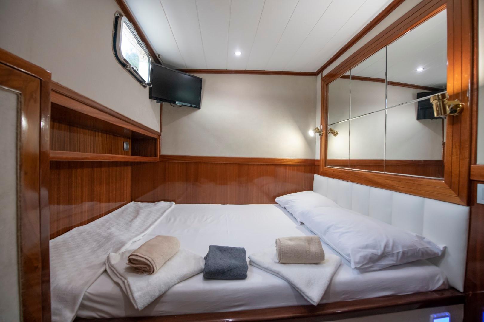 yacht guest cabin interior with double bed white linens wood paneling and flat screen TV