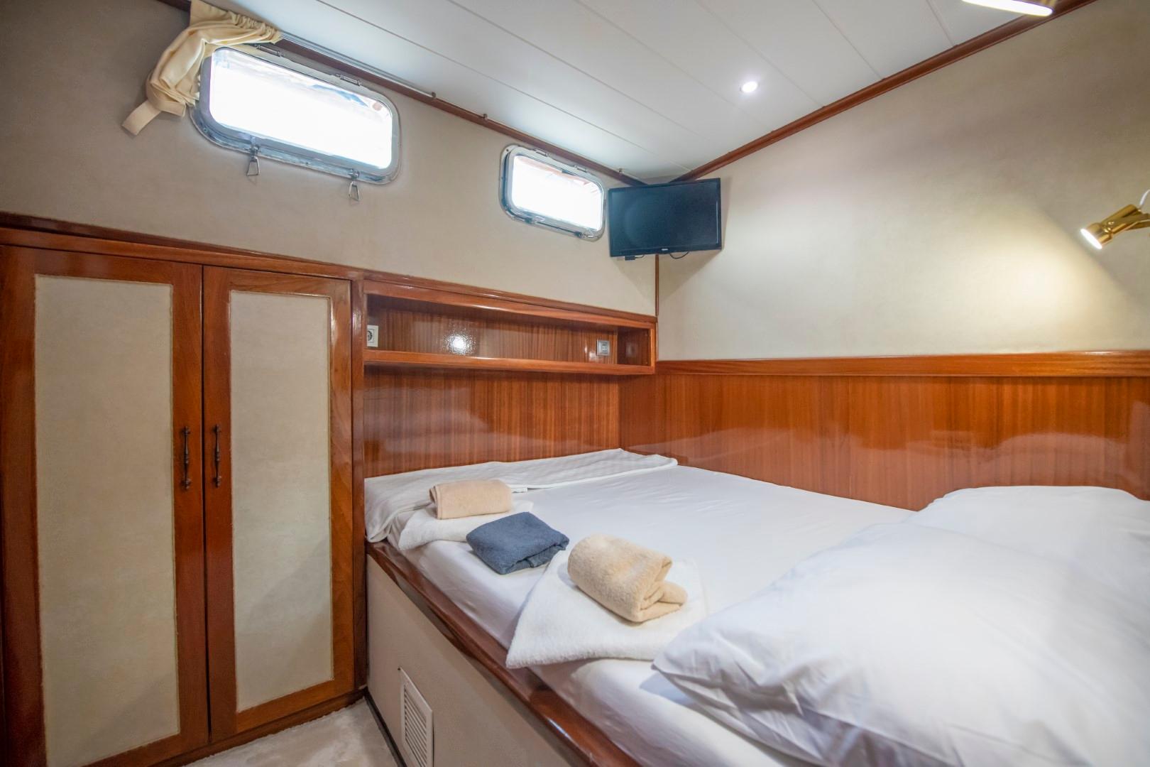 yacht guest cabin featuring double bed with white linens, wooden built-in wardrobes, portholes and wall-mounted TV