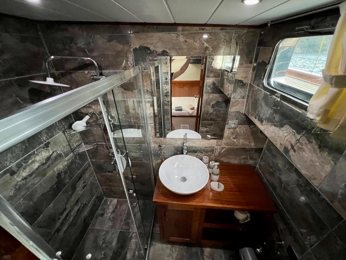 luxury yacht bathroom featuring dark marble walls, glass shower enclosure, and vessel sink