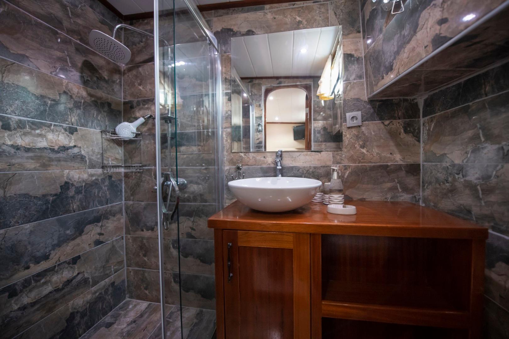 luxury yacht bathroom featuring marble tile walls, glass shower enclosure, and wooden vanity with vessel sink