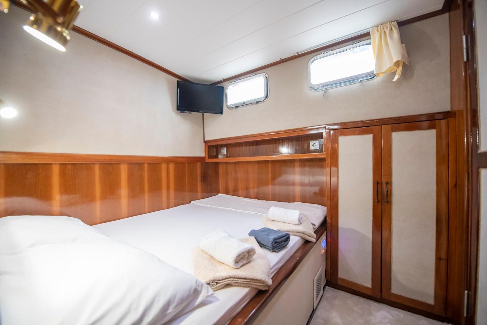 yacht guest cabin featuring twin beds with white linens, wood paneling, portholes and built-in wardrobes