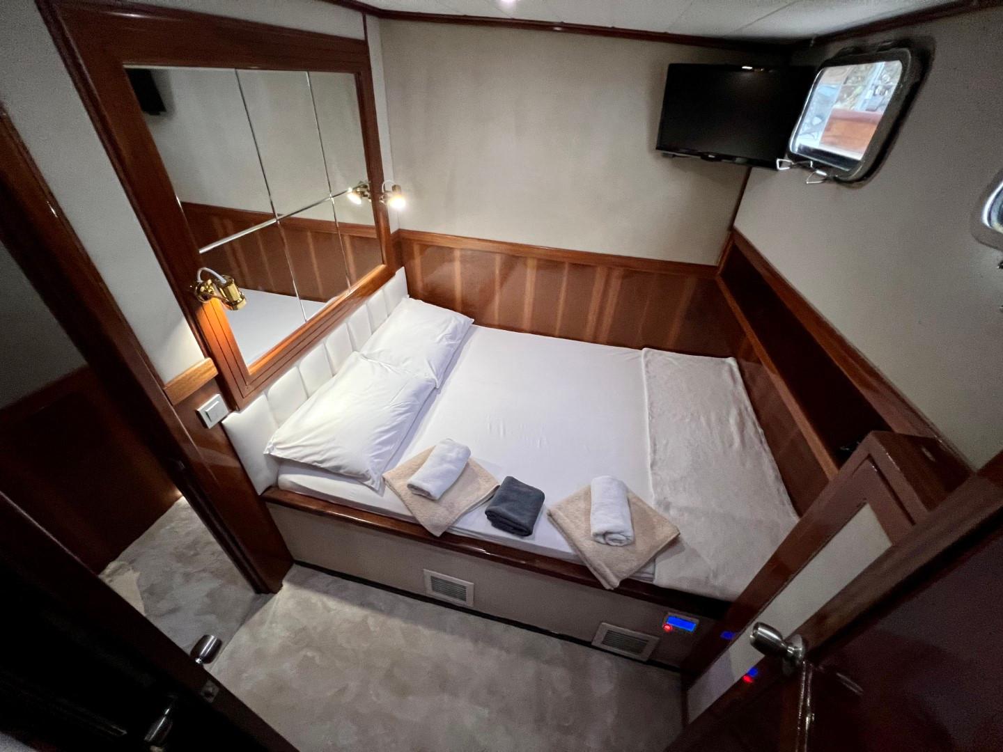 yacht guest cabin featuring double bed with white bedding, wooden paneling, wall-mounted TV and porthole window