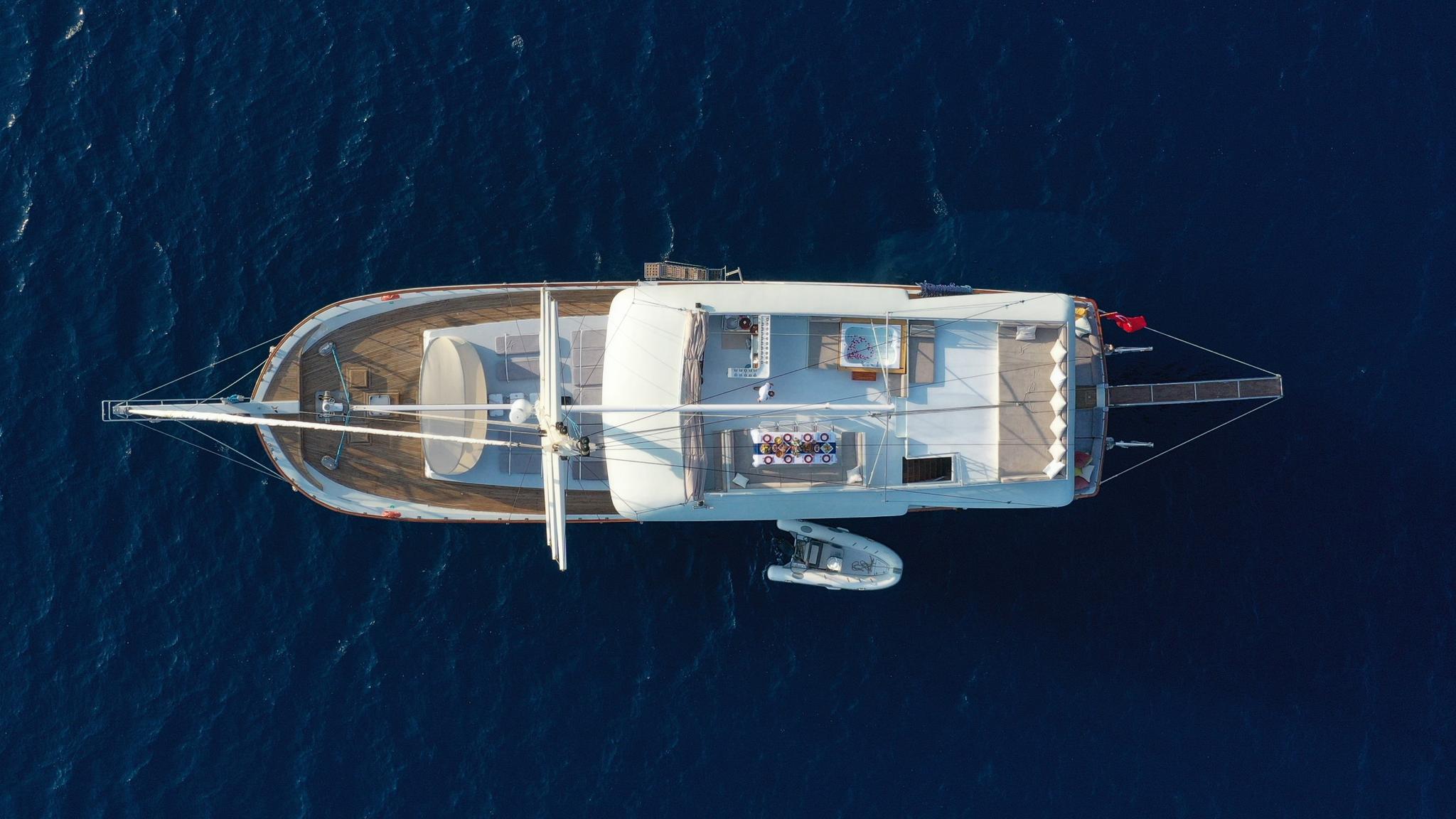 aerial view of white luxury gulet yacht at anchor with tender alongside in deep blue Mediterranean waters