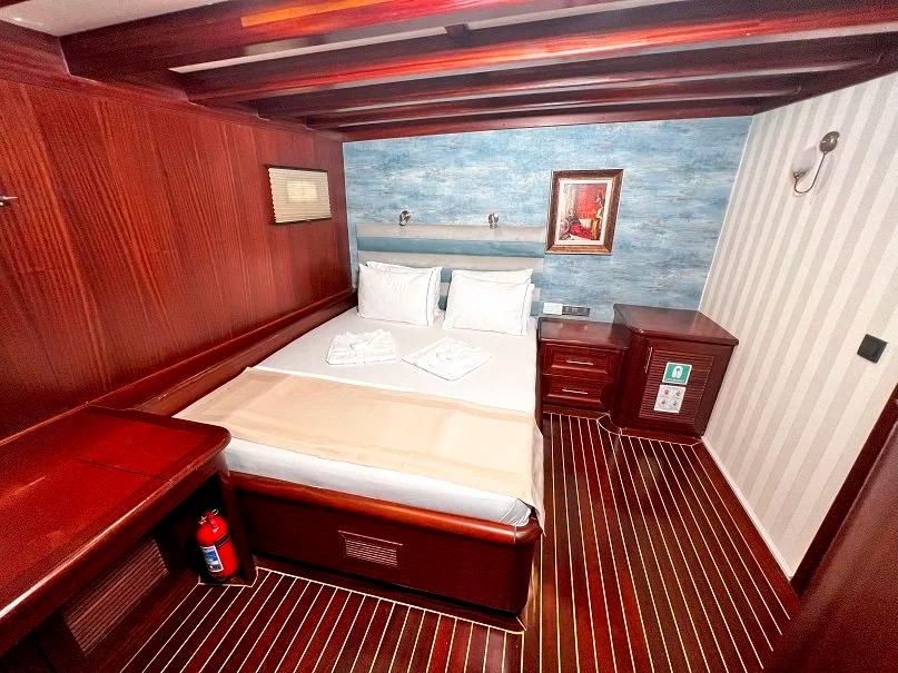 yacht guest cabin featuring double bed with white linens, rich mahogany wood paneling, and nautical artwork