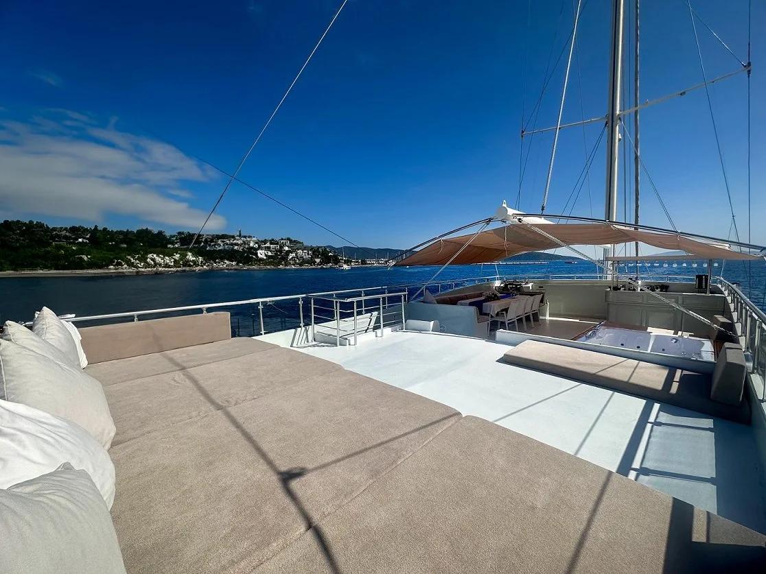aft deck with beige cushioned seating, white awning, and Mediterranean coastline views