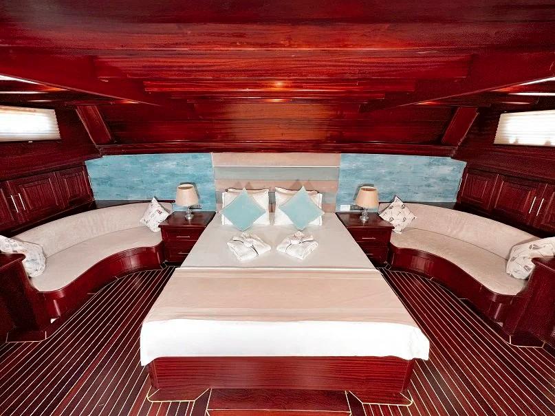 luxury yacht master cabin featuring double bed with white linens, curved seating areas, mahogany woodwork and portholes