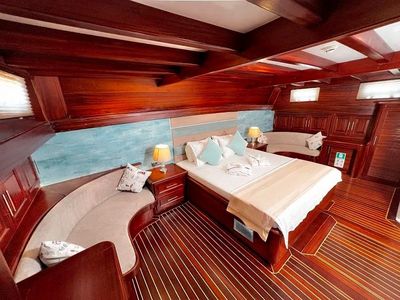 master cabin featuring king bed, curved seating area, panoramic windows and rich wood paneling