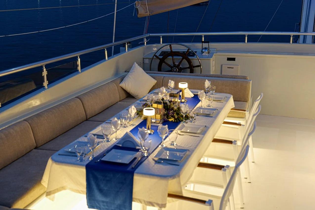 aft deck dining table formally set with blue runner, white chairs and helm station behind