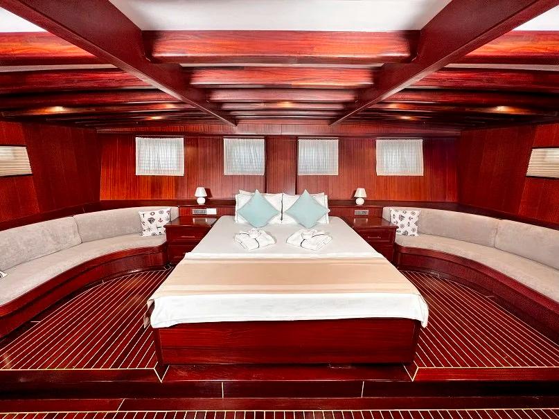 Luxury yacht master cabin featuring king bed, curved bench seating, rich mahogany woodwork and four portholes