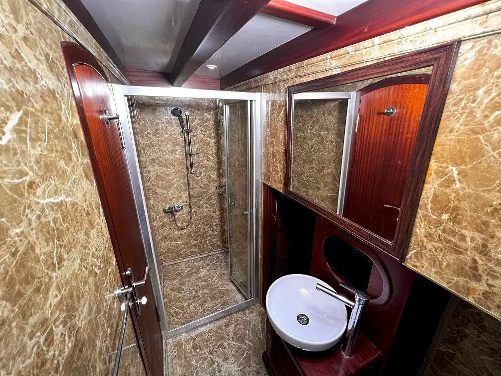 luxury yacht bathroom featuring glass shower enclosure, marble walls, and wooden vanity with round basin
