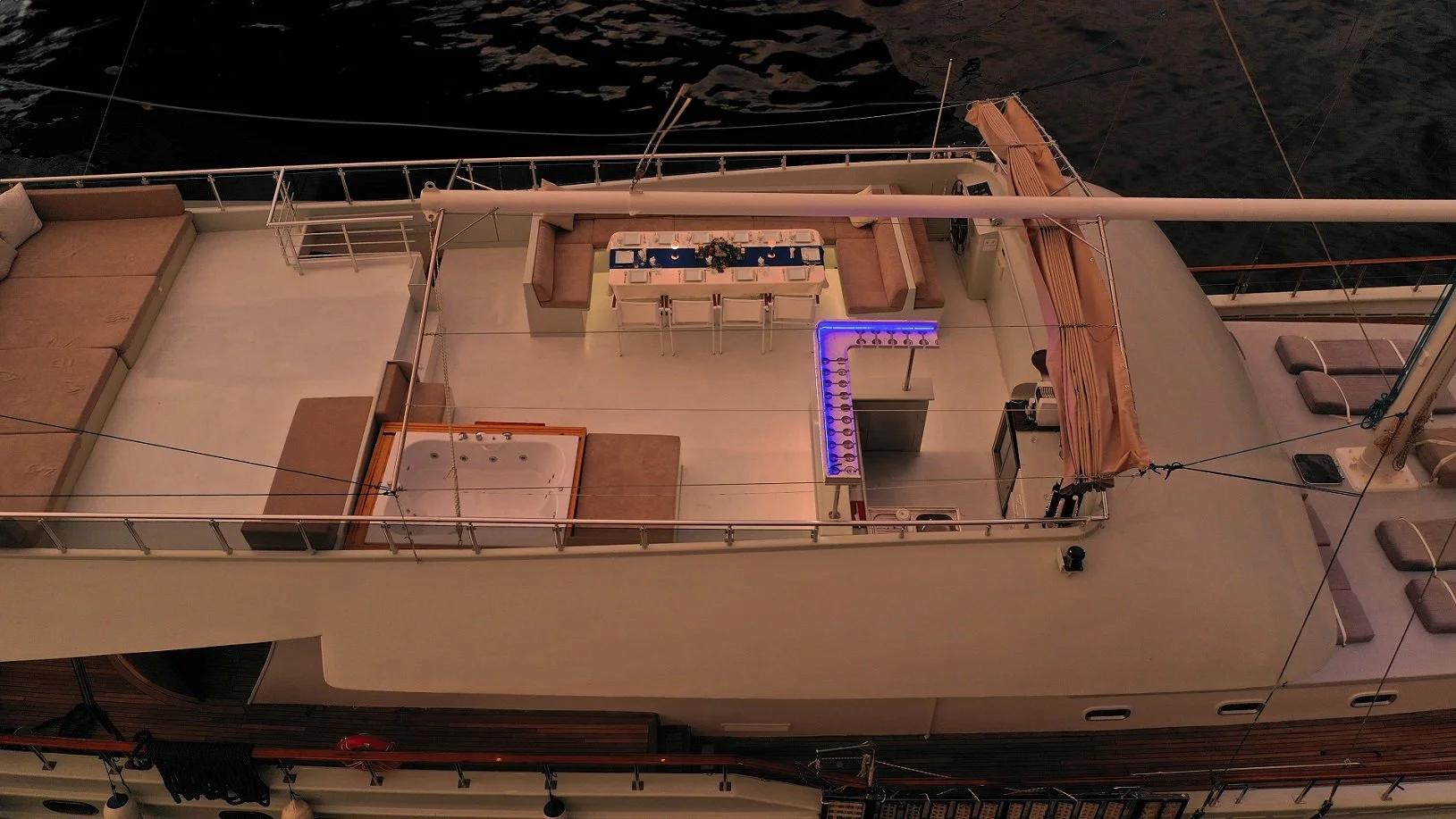 aerial night view of luxury yacht deck showing jacuzzi, dining area and purple LED lighting