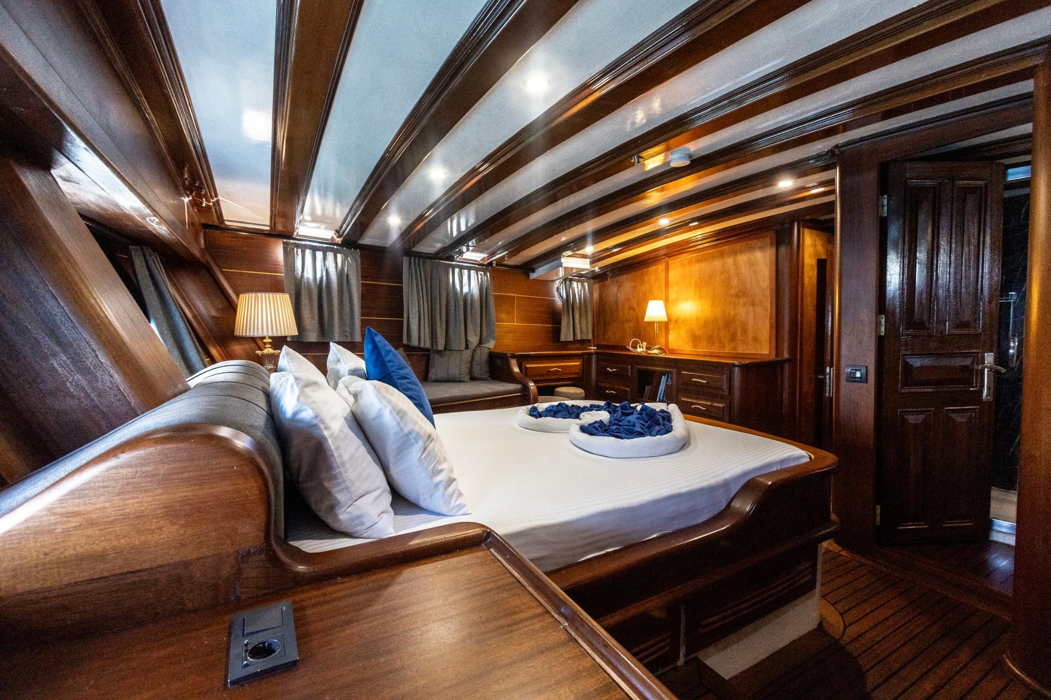 yacht guest cabin featuring double bed with white linens, exposed wooden ceiling beams, and built-in furniture