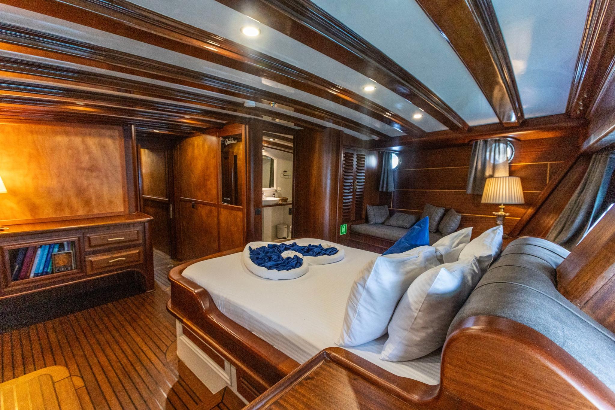 yacht guest cabin featuring double bed, wooden paneling, built-in seating and en-suite bathroom