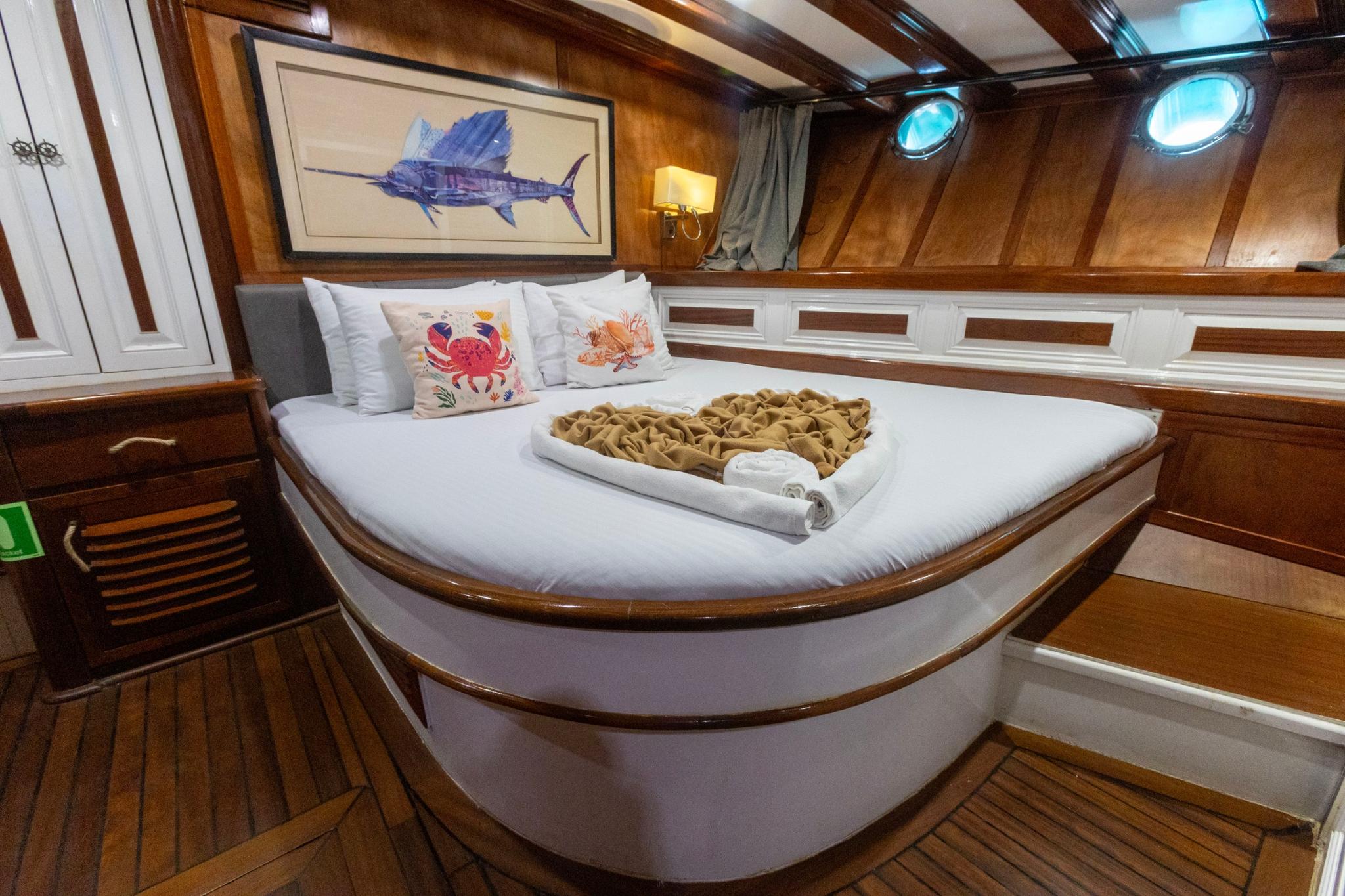 Guest cabin featuring double bed with white linens, sailfish artwork, portholes and wooden paneling
