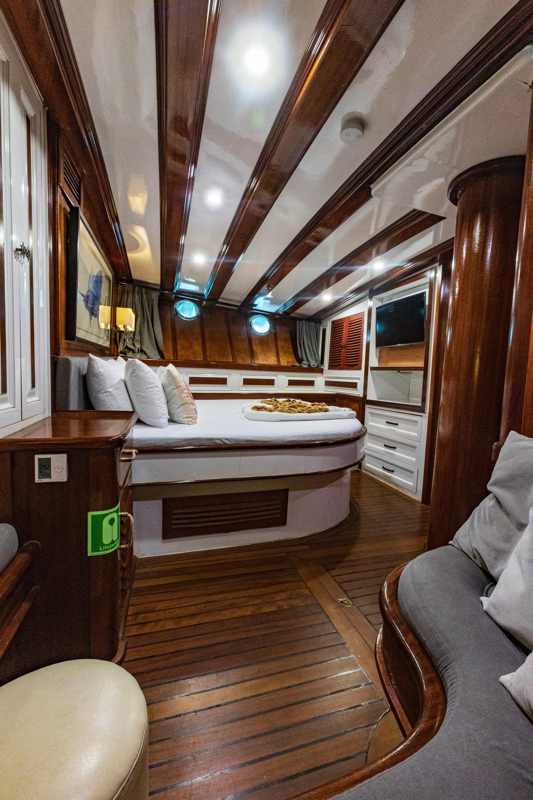 yacht cabin with double bed, built-in storage, seating bench and wooden ceiling beams