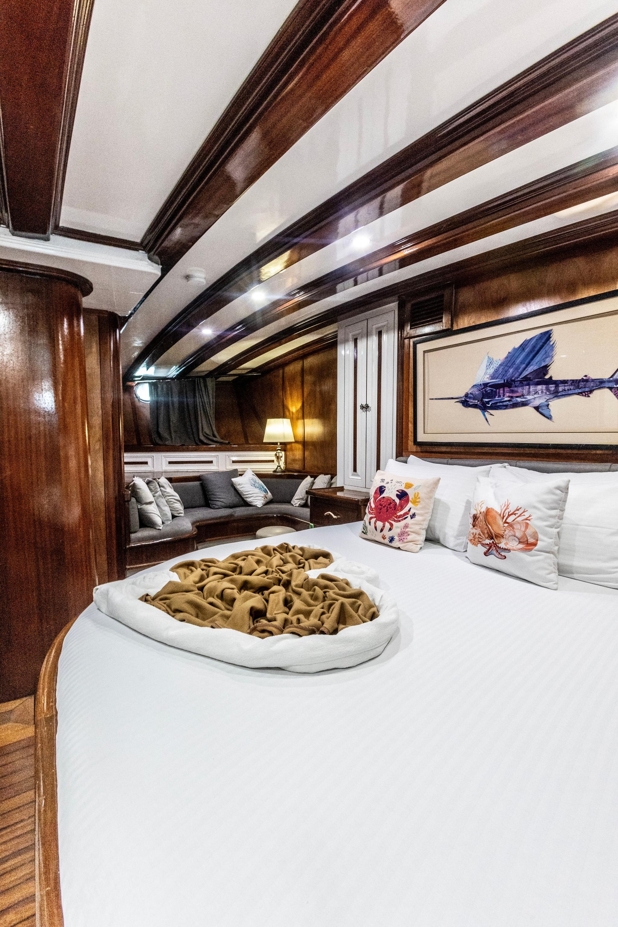 luxury yacht master cabin featuring king bed, exposed wooden beams, nautical artwork and seating area